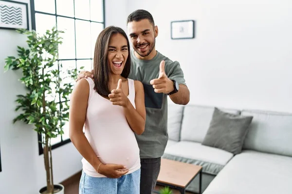 Young interracial couple expecting a baby, touching pregnant belly pointing fingers to camera with happy and funny face. good energy and vibes.