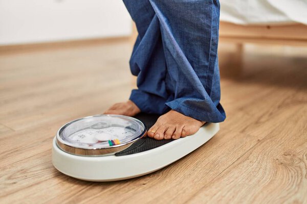 Middle age caucasian woman using weighing machine at home
