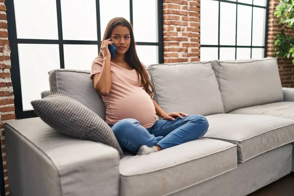 Young pregnant woman having conversation speaking on the smartphone thinking attitude and sober expression looking self confident