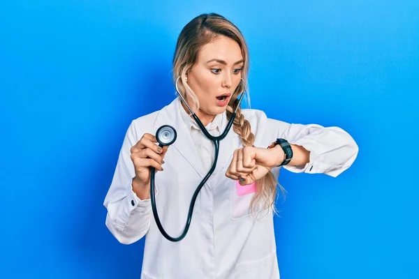 Beautiful Young Blonde Doctor Woman Holding Stethoscope Looking Watch Time — 스톡 사진