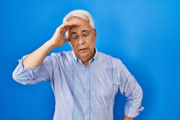 Hispanic senior man wearing glasses worried and stressed about a problem with hand on forehead, nervous and anxious for crisis