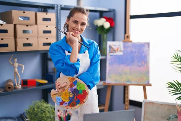 Young woman artist holding paintbrush and palette at art studio