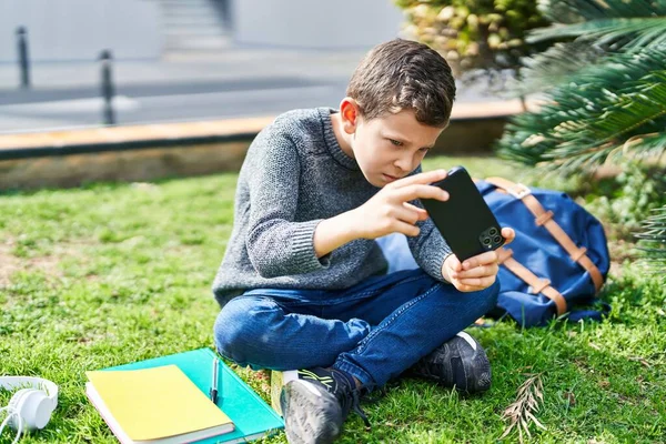 金发小孩坐在公园的草地上玩电子游戏 — 图库照片