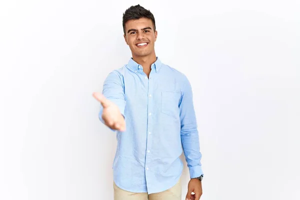 ビジネスシャツを着た若いヒスパニック系の男が孤立した背景に立って笑顔陽気にヤシの手を提供支援し 受け入れ — ストック写真