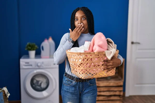 African American Woman Holding Laundry Basket Covering Mouth Hand Shocked —  Fotos de Stock