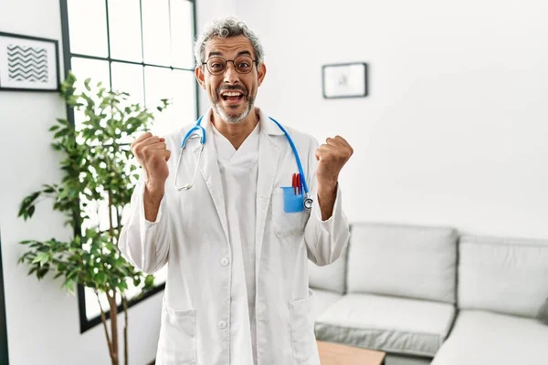 中年惊慌失措的男人身穿医生制服和听诊器 站在候车室庆祝成功 惊讶地举起双臂睁开眼睛 获奖者概念 — 图库照片