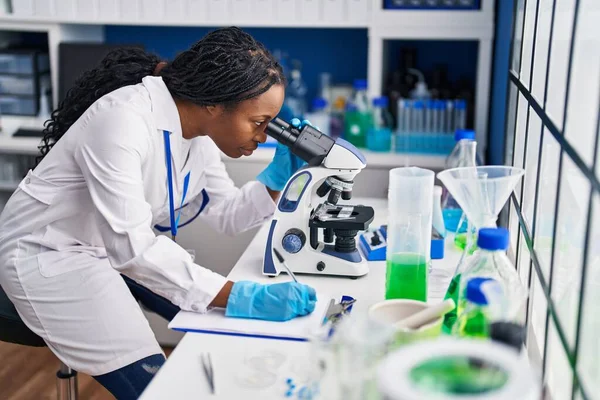 African American Woman Wearing Scientist Uniform Writing Clipboard Using Microscope — ストック写真