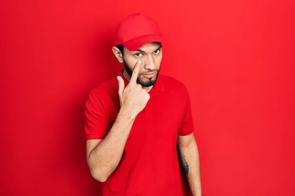 Hispanic Man Beard Wearing Delivery Uniform Cap Pointing Eye Watching — Zdjęcie stockowe