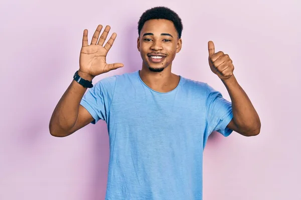 自信と幸せ笑みを浮かべている間若いアフリカ系アメリカ人の男性は カジュアルな青のTシャツを着て指の数6を示すと指摘 — ストック写真