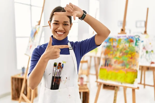 Young brunette woman at art studio smiling making frame with hands and fingers with happy face. creativity and photography concept.