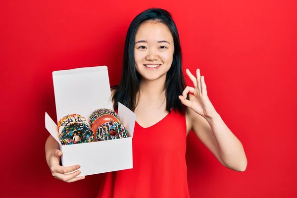 Young Chinese Girl Holding Box Tasty Colorful Doughnuts Doing Sign — Foto Stock