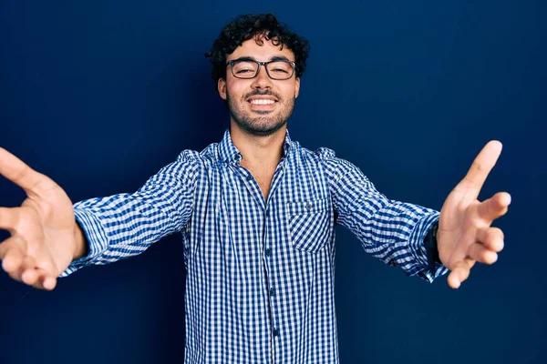 カジュアルな服を着てカメラを見ている若いヒスパニック系の男が抱擁のために腕を開いて笑っている 幸せを受け入れる陽気な表情 — ストック写真