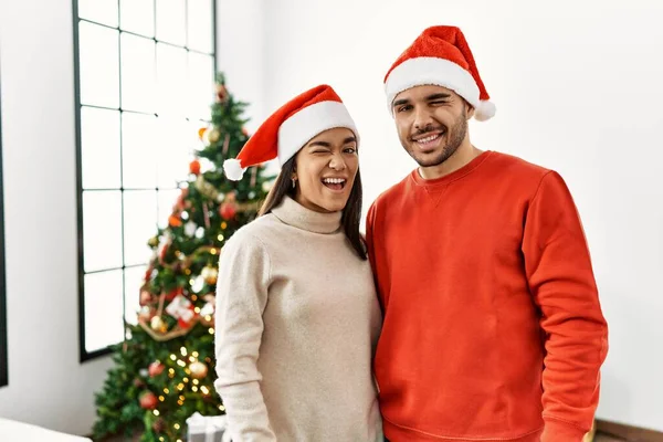 他的一对年轻夫妇站在圣诞树旁眨着眼睛 带着性感的表情 笑容满面地看着摄像机 — 图库照片