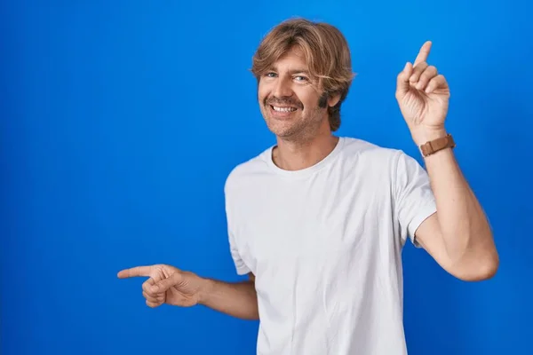 青い背景の上に立つ中年の男性は さまざまな方向に指で自信を持って指して笑顔 広告のコピースペース — ストック写真