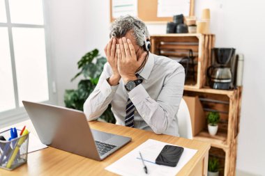 Ofiste çalışan orta yaşlı bir İspanyol işadamı operatör kulaklığı takıyor ve ağlarken yüzünü ellerle kapatıyor. depresyon kavramı. 