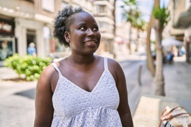 Genç Afrikalı Amerikalı kadın gülümseyerek şehirde mutlu mesut duruyor..