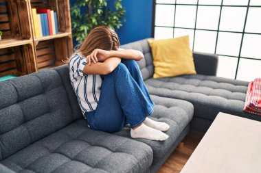 Evdeki kanepede oturan genç sarışın kadın depresyonda.