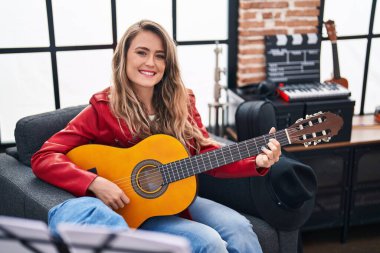 Young woman musician playing classical guitar at music studio
