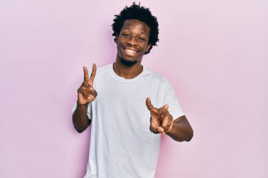 Gündelik beyaz tişört giyen genç Afro-Amerikan adam kameraya bakıp zafer işareti yapıyor. İki numara.. 