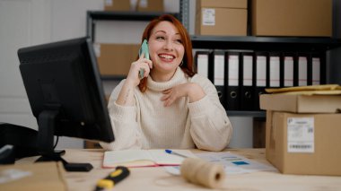 Genç kızıl saçlı kadın iş kadını ofisteki akıllı telefondan konuşuyor.