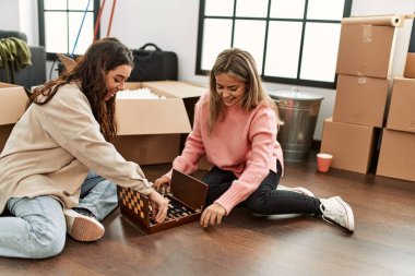 Genç çift yeni evinde yerde oturup satranç oynarken mutlu bir şekilde gülümsüyor..