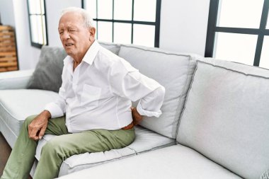 Senior man suffering for backache sitting on sofa at home