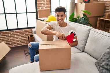 Genç İspanyol adam yeni evinde kendine güvenen bir karton kutu paketliyor.