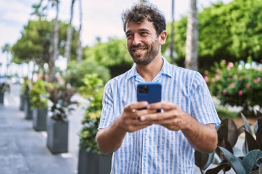 Genç İspanyol adam şehirde akıllı telefon kullanarak mutlu gülümsüyor..