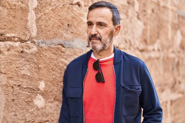 Orta yaşlı, rahat yüzlü bir adam sokakta dikiliyor.