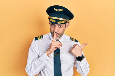 Gri saçlı, uçak pilotu üniforması giyen yakışıklı orta yaşlı bir adam ellerini yana uzatarak parmaklarını dudaklarına dayayıp sessiz olmak istiyor. sessizlik ve gizli konsept. 