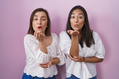 Hispanic mother and daughter together looking at the camera blowing a kiss with hand on air being lovely and sexy. love expression. 