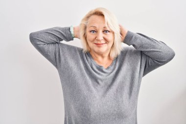 Middle age caucasian woman standing over white background relaxing and stretching, arms and hands behind head and neck smiling happy 