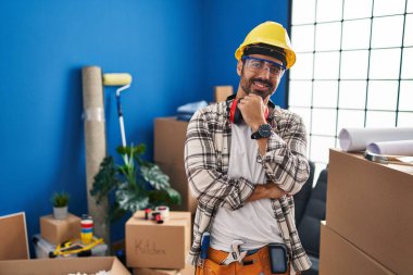 Sakallı, ev tadilatında çalışan genç İspanyol adam kameraya bakıyor kollarını kavuşturmuş ve çenesini kaldırmış gülümsüyor. Olumlu düşünmek. 