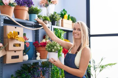 Çiçekçide çiçek tutan, gülümseyen genç sarışın kadın.