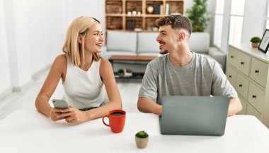 Kafkasyalı genç çift kahve içiyor ve evde dizüstü bilgisayar ve akıllı telefon kullanıyor..