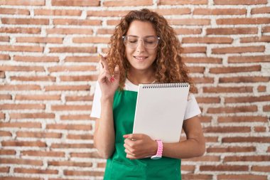 Sanat defteri tutan beyaz bir kadın umut ve gözlerin kapalı bir şekilde gülümseyerek işaret ediyor. Şans ve batıl inançlar. 