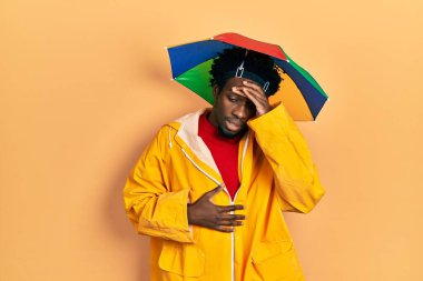 Sarı yağmurluk giyen genç Afro-Amerikalı adam hastalık, ateş, grip ve soğuk algınlığı için alnına dokunuyor. 