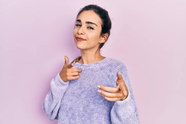 Günlük kıyafetler giyen genç İspanyol kız mutlu ve komik yüzüyle kamerayı işaret ediyor. iyi enerji ve titreşimler. 