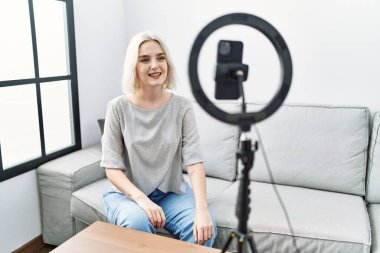Young caucasian woman recording vlog tutorial with smartphone at home with a happy and cool smile on face. lucky person. 