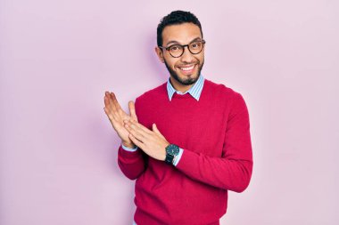 Hispanic man with beard wearing business shirt and glasses clapping and applauding happy and joyful, smiling proud hands together 