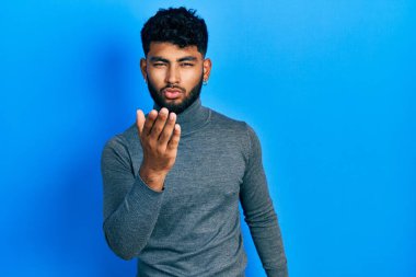 Arab man with beard wearing turtleneck sweater looking at the camera blowing a kiss with hand on air being lovely and sexy. love expression. 