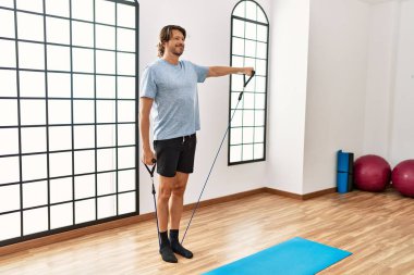 Middle age caucasian man smiling confident training using elastic band at sport center