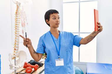 Fizyoterapi kliniğinde, fizyoterapi kliniğinin omurgasını gösteren video mesajı alan, fizyoterapist üniformalı genç bir kadın.