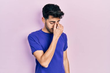 Gündelik tişört giyen genç İspanyol adam yorgun burnu ve gözleri ovuşturup yorgunluk ve baş ağrısı hissediyor. Stres ve hüsran kavramı. 