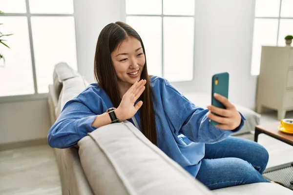 年轻的中国女孩有视频 坐在家里沙发上 用智能手机打电话 — 图库照片