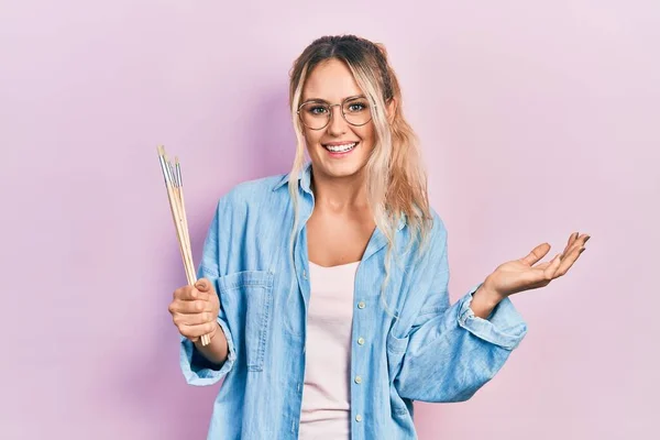 Beautiful Young Blonde Woman Holding Paintbrushes Celebrating Achievement Happy Smile — Stok fotoğraf