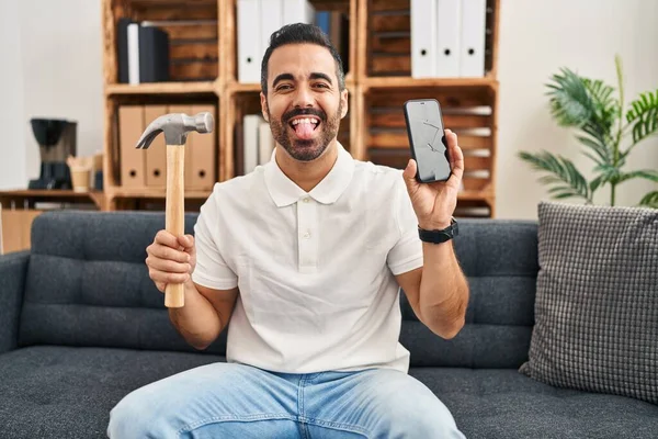 Jovem Hispânico Homem Com Barba Segurando Martelo Smartphone Quebrado Mostrando — Fotografia de Stock