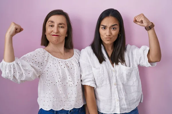 Hispanic mother and daughter together strong person showing arm muscle, confident and proud of power