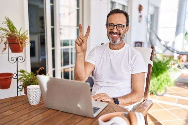 Middle age man using computer laptop at home showing and pointing up with fingers number two while smiling confident and happy.