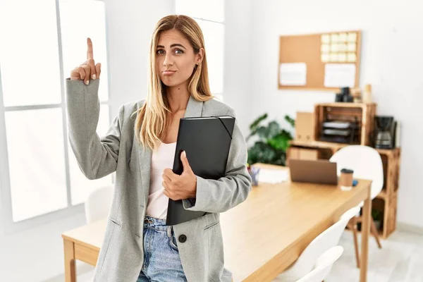 Blonde business woman at the office pointing up looking sad and upset, indicating direction with fingers, unhappy and depressed.